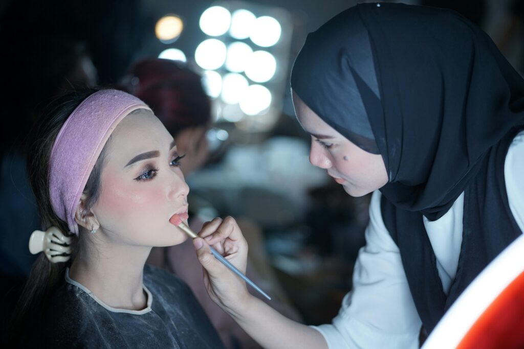 A makeup artist applying lipstick to a model in a beauty studio setting.