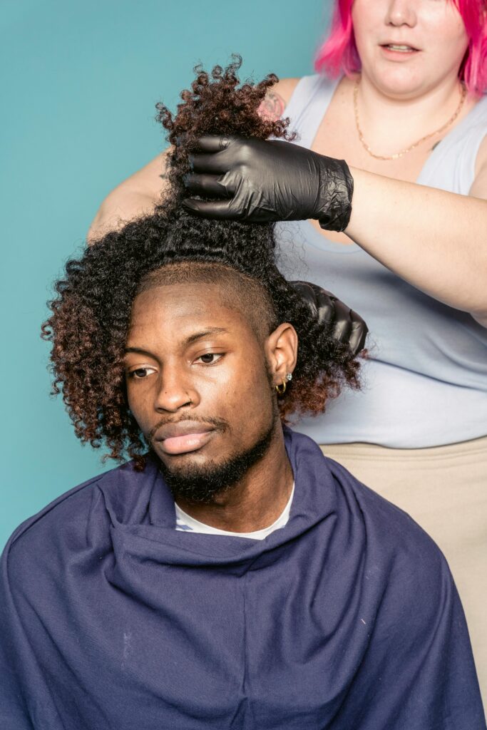 Crop female hairstylist doing curly hair of African American male client against blue background