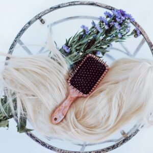 Blonde wig styled with brush and purple flowers on a round table, showcasing hair beauty and care.